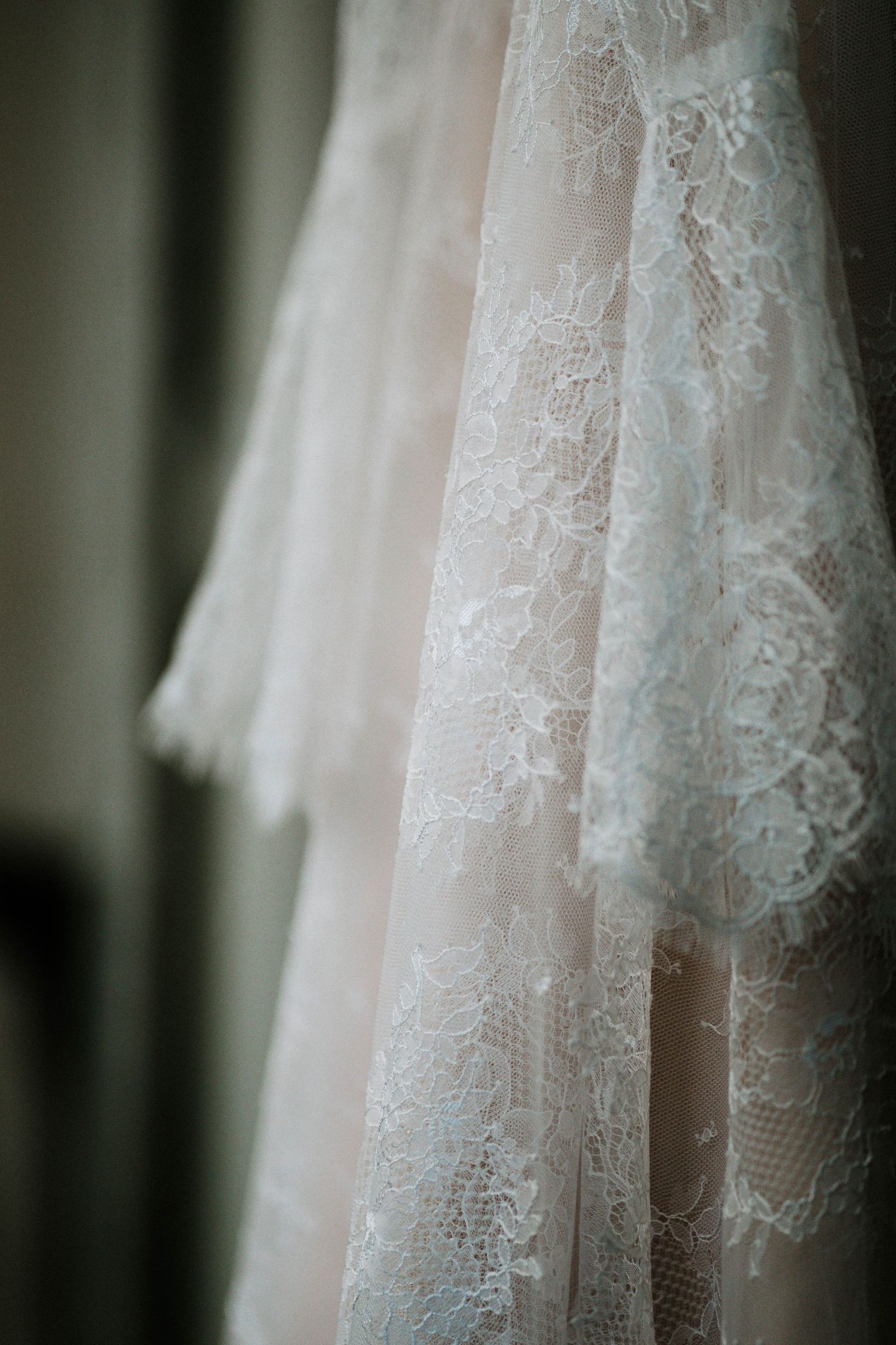 Close-up of elegant white lace wedding dress layers hanging, showcasing intricate floral lace patterns and delicate fabric texture.