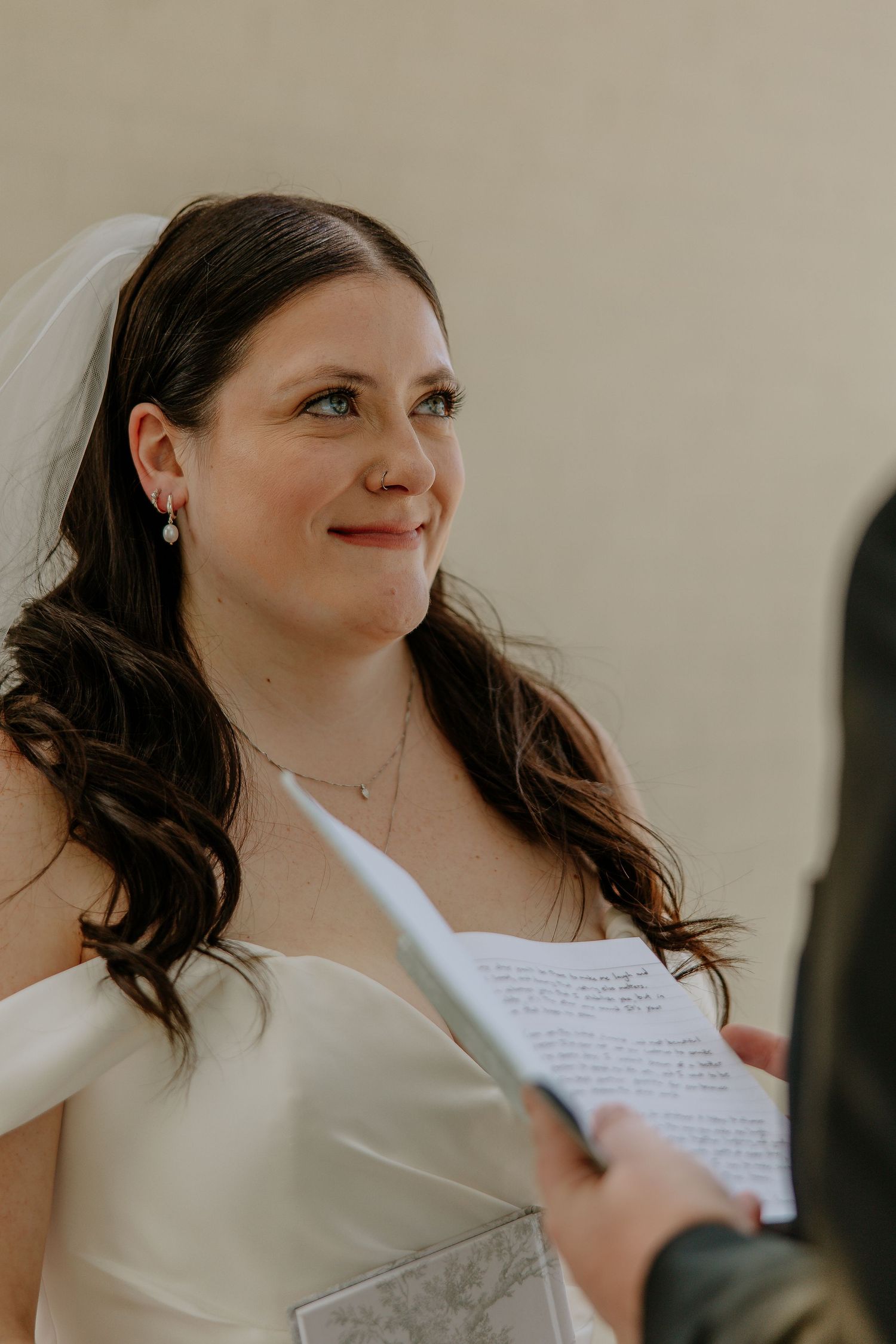 Close-up of emotional bride listening to wedding vows, wearing pearl earrings and delicate veil.