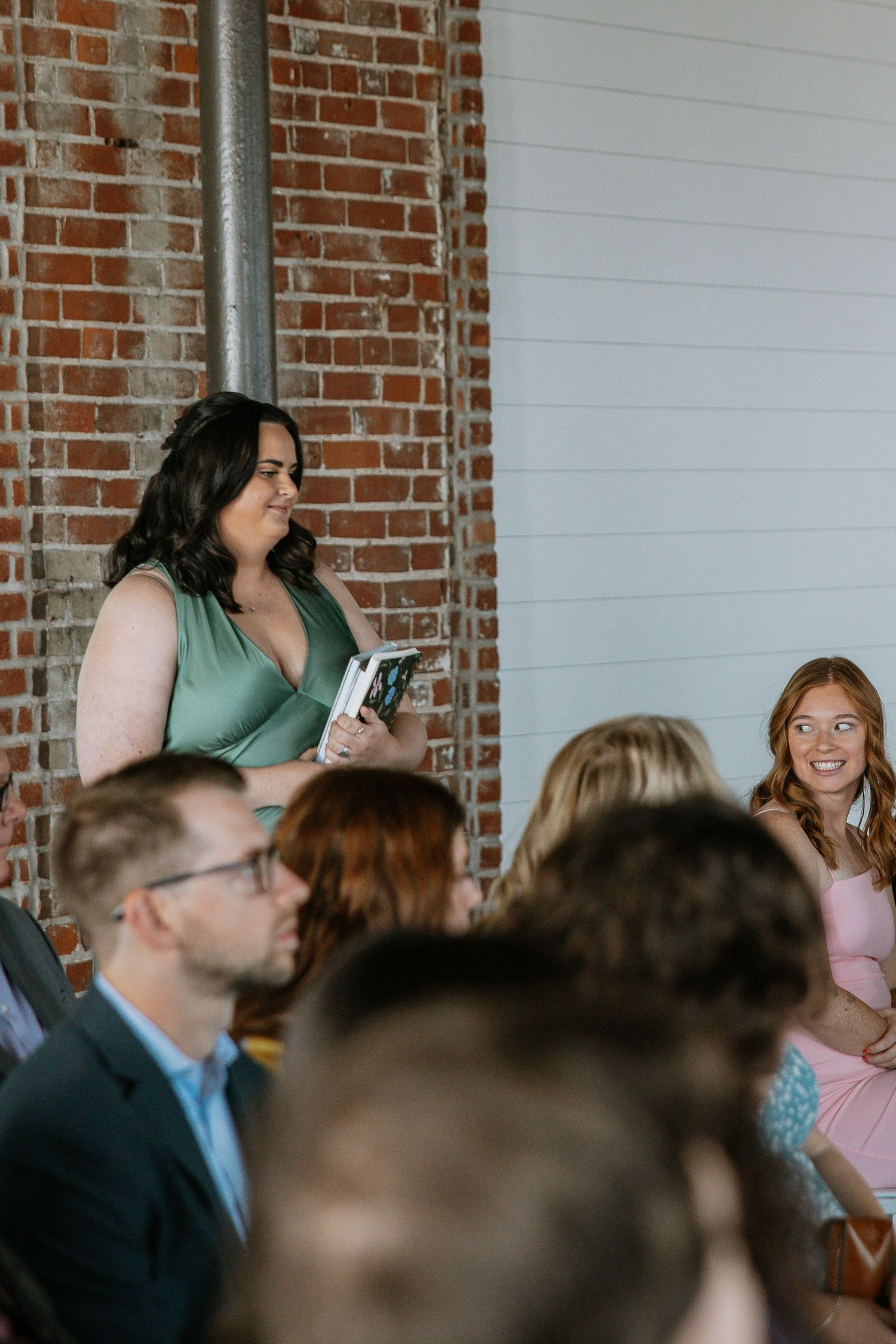 Woman in green floral dress holding a book and speaking at a wedding ceremony.