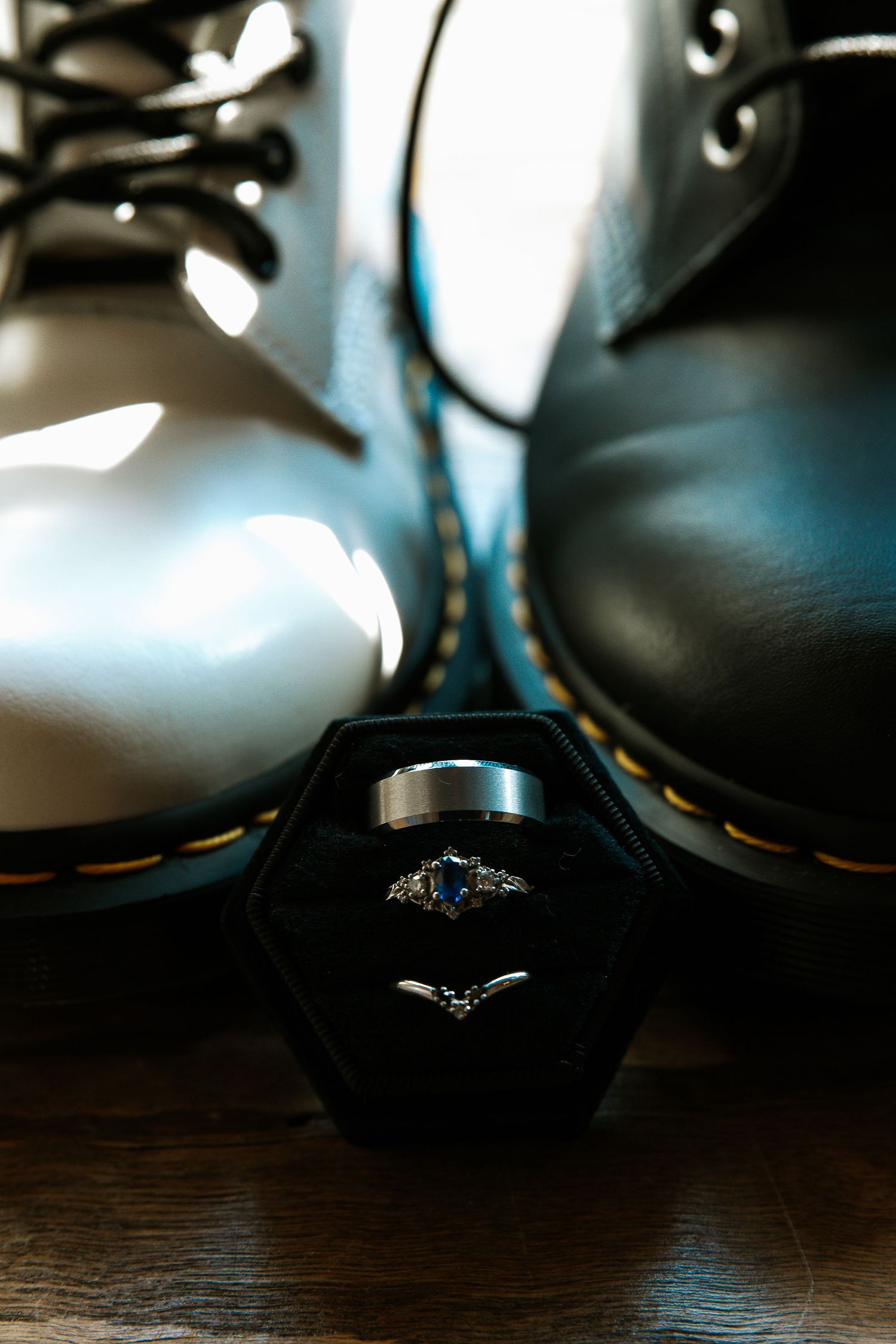 Wedding rings displayed in black velvet box between white and black Dr. Martens boots on wooden floor.