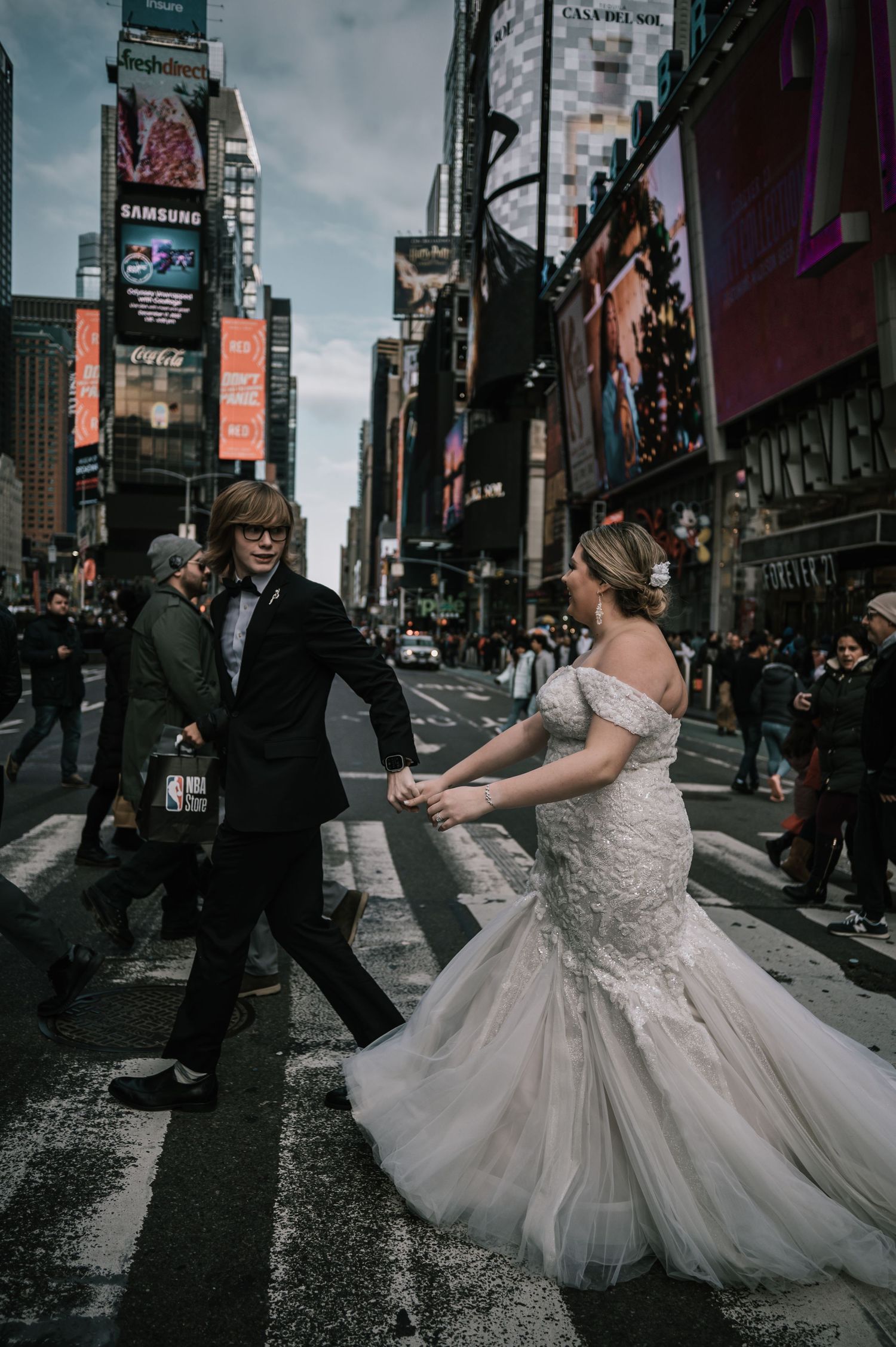 Bride and groom holding hands crossing Times Square in New York City on their wedding day.