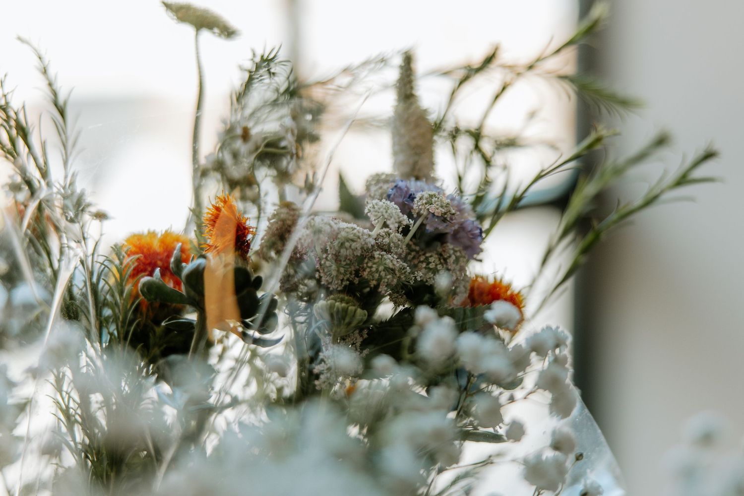 Close-up of a rustic wedding floral arrangement with orange, white, and purple wildflowers.