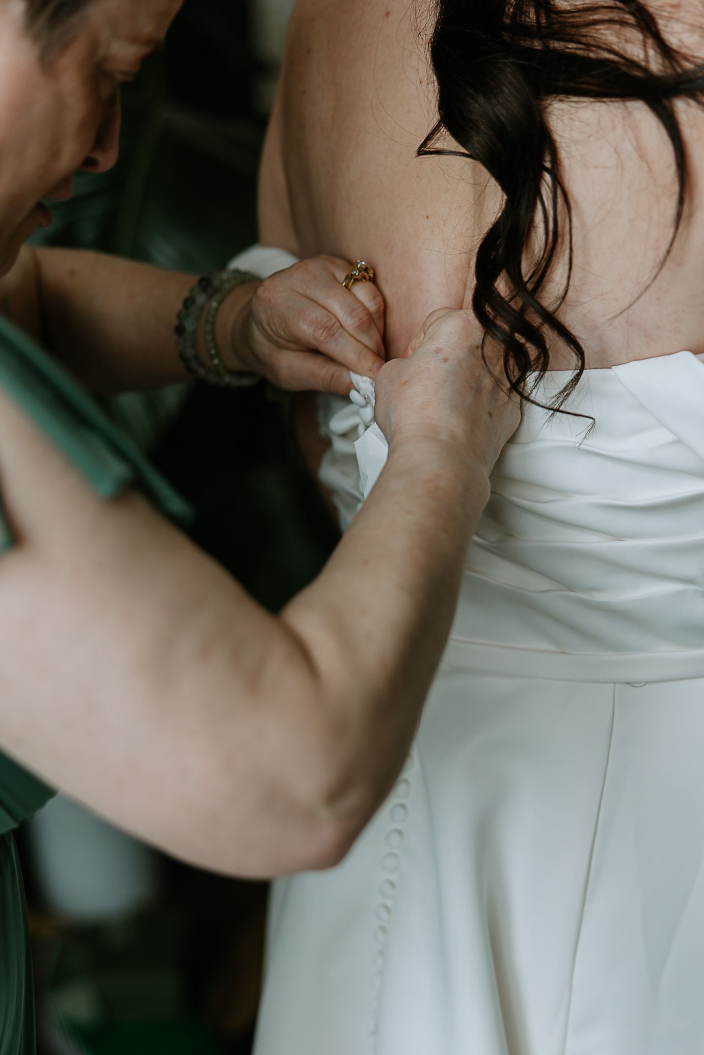 Mother of the bride carefully adjusting the back of her daughter's white wedding gown.