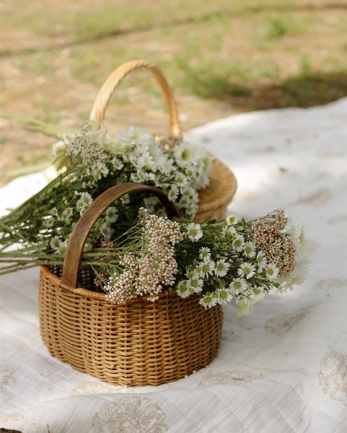 Two wicker baskets filled with white wildflowers and baby's breath on a white cloth outdoors in Cincinnati, Ohio.