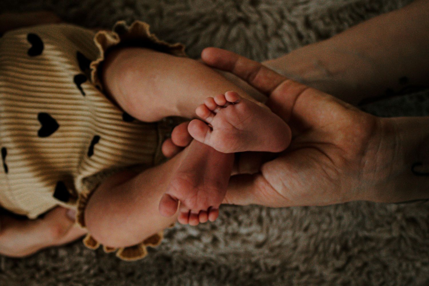 Adult hands gently cradling tiny newborn baby feet on a soft gray blanket at Mill Street Studios in Cincinnati, Ohio.