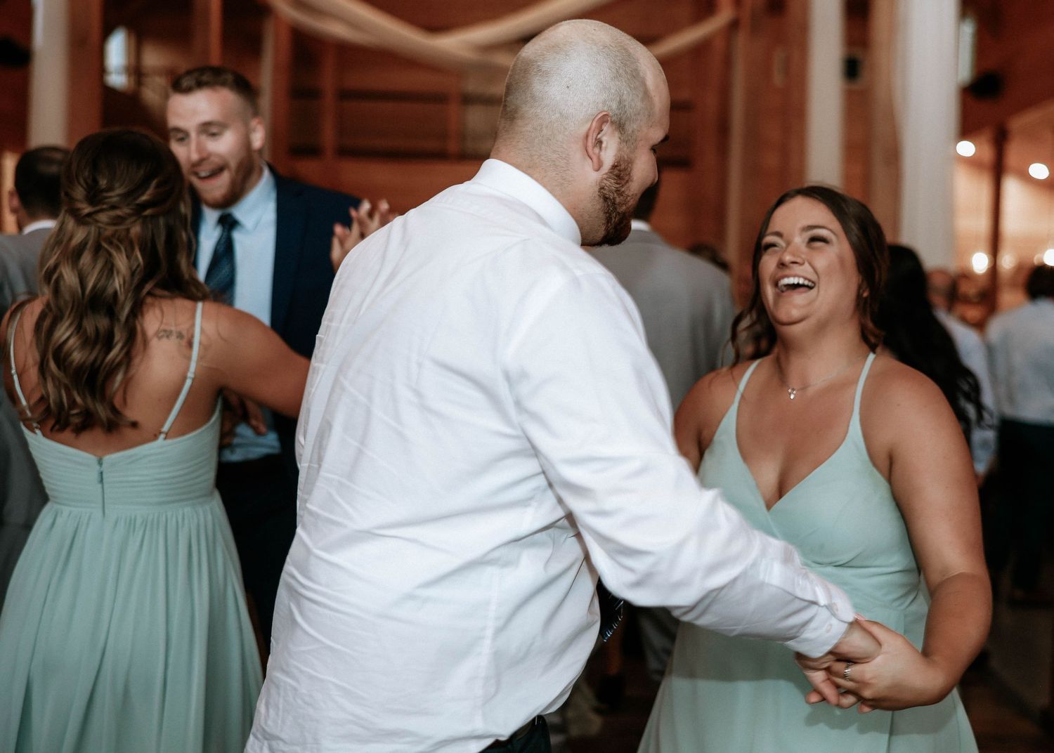Guests dancing and laughing at a wedding reception, woman in mint green dress smiling joyfully.