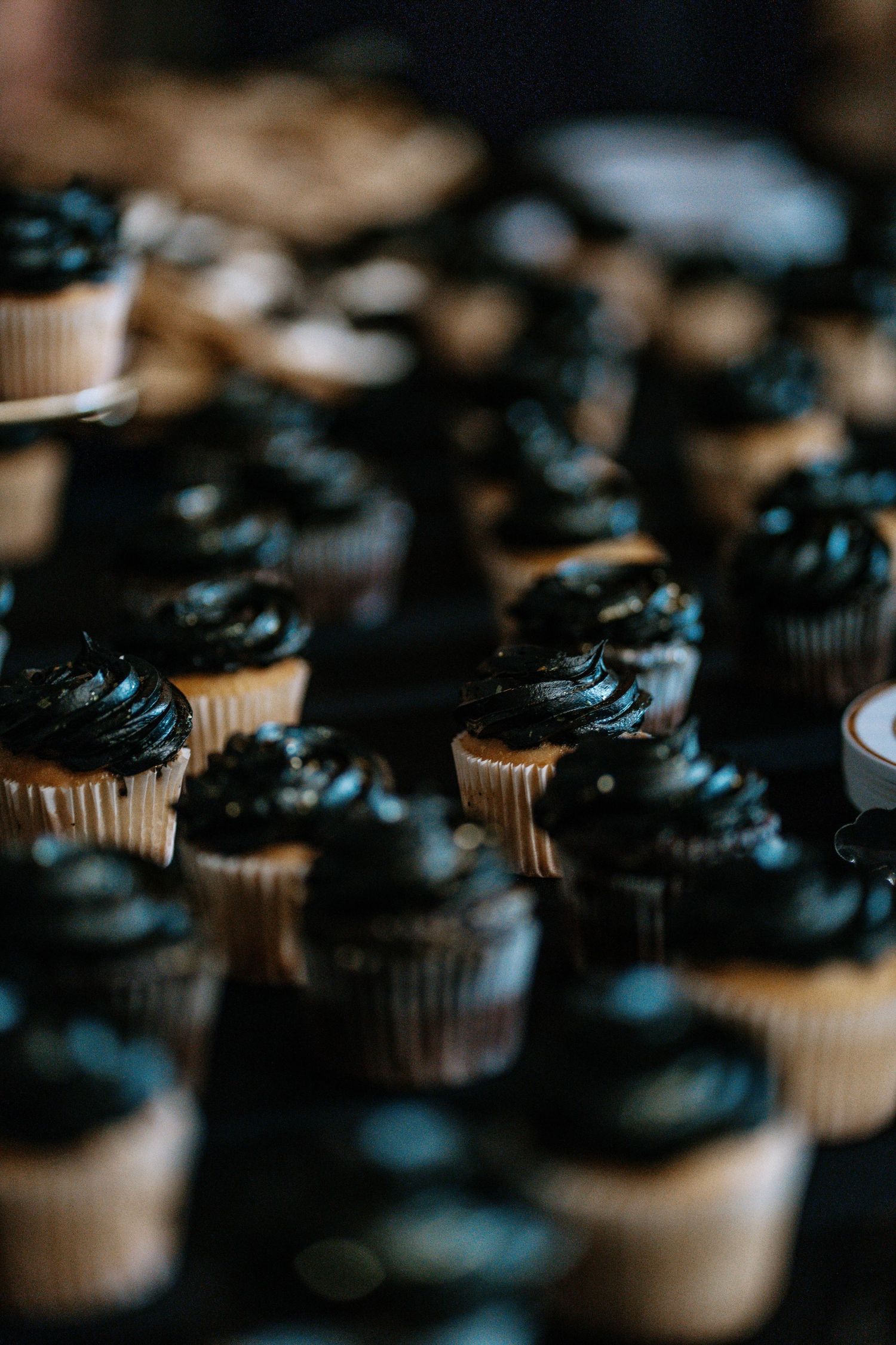 Rows of cupcakes with dark black frosting swirls in white paper liners arranged on a table.