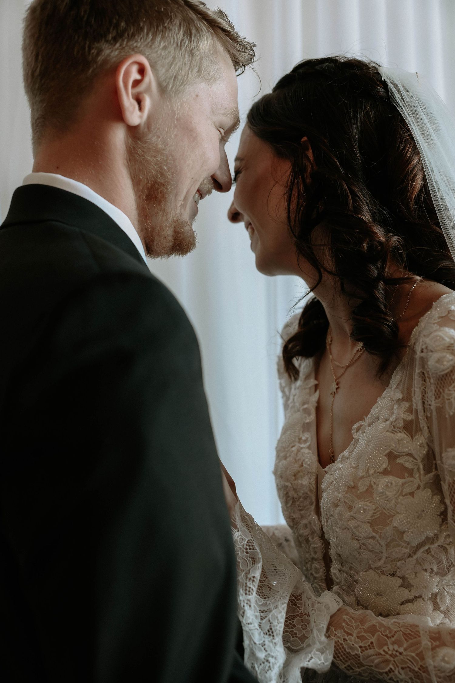 Bride and groom share an intimate moment, touching foreheads and smiling on their wedding day.