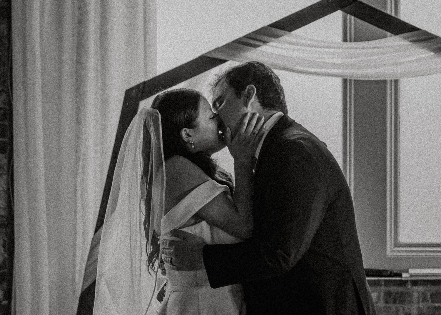 Black and white photo of bride and groom kissing at wedding ceremony.