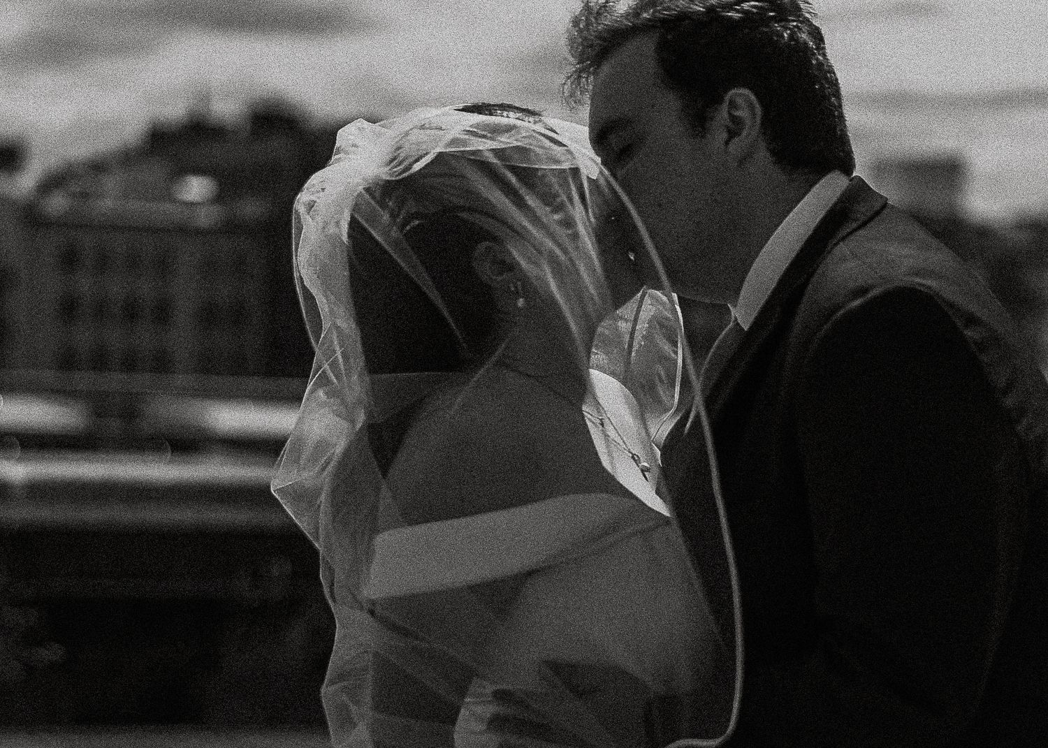 Romantic black and white photo of bride and groom kissing, bridal veil flowing around them.