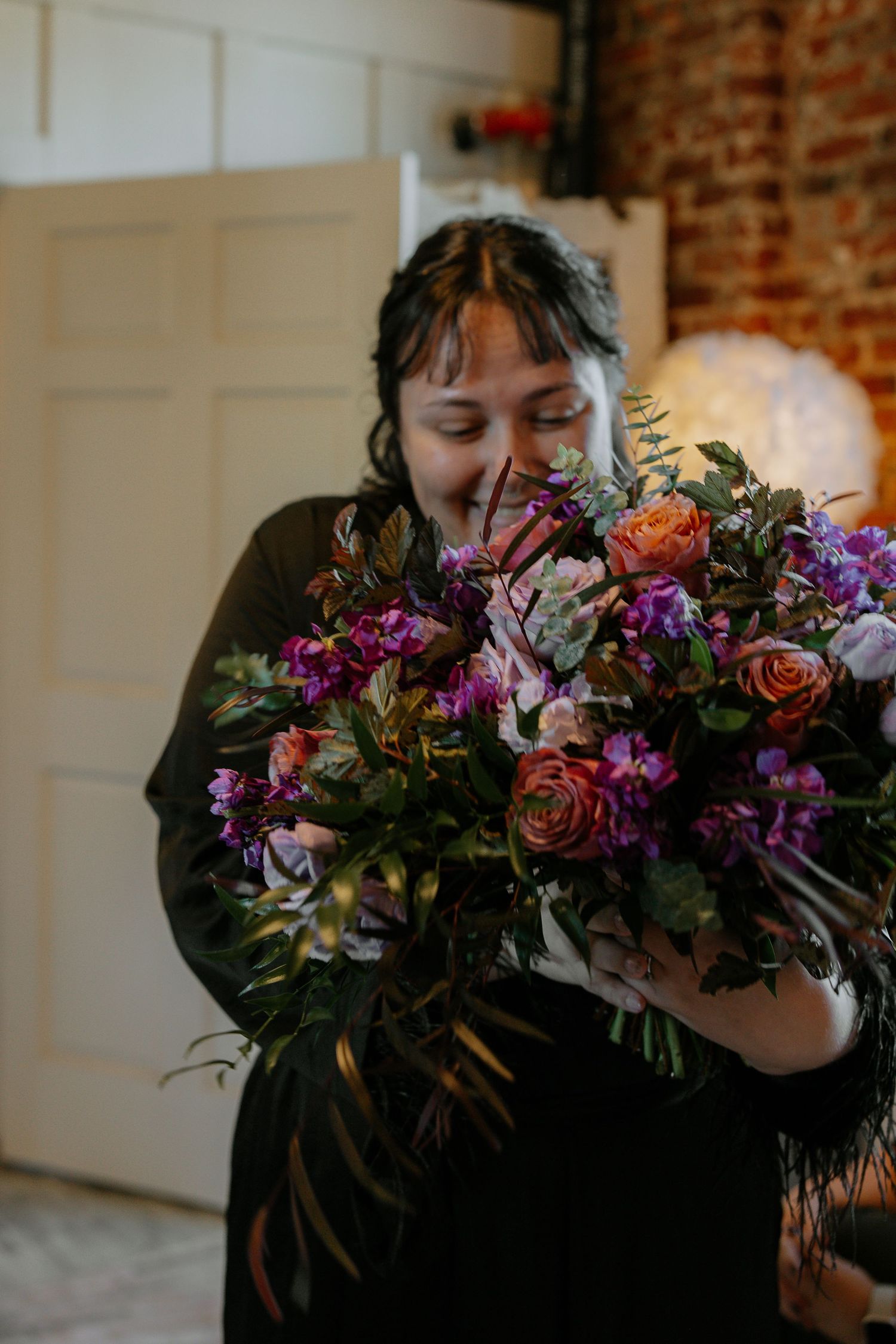 Bride smells a vibrant purple and orange wedding bouquet while smiling.