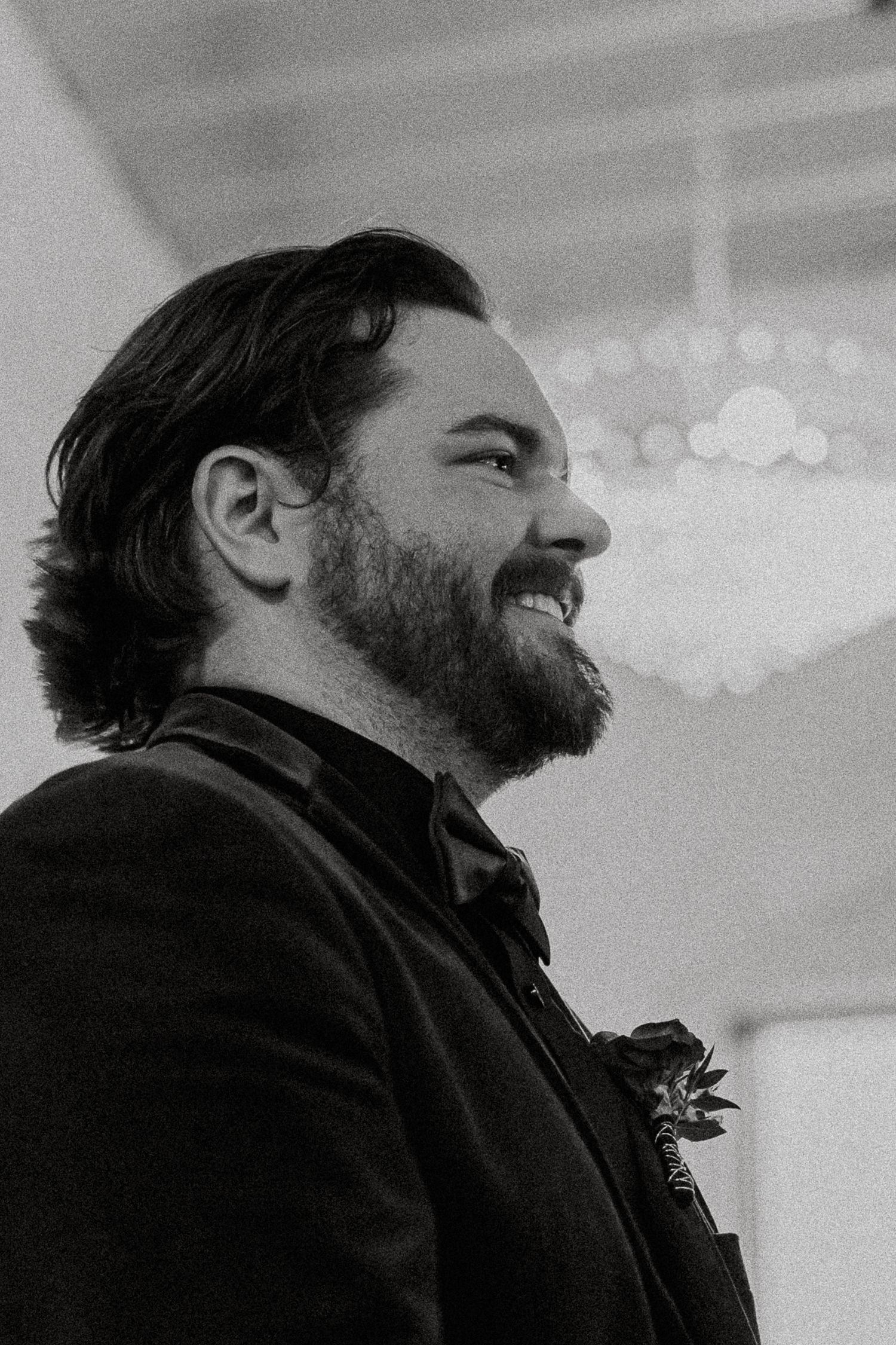 Black and white close-up of bearded groom smiling joyfully during wedding ceremony.