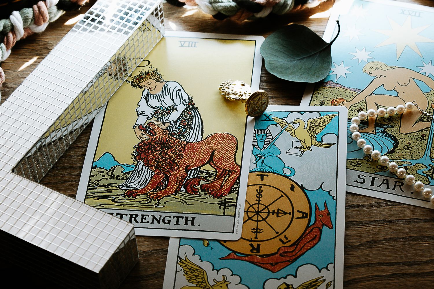 Tarot cards including Strength and the Star spread on wooden table with pearl jewelry and decorative items.