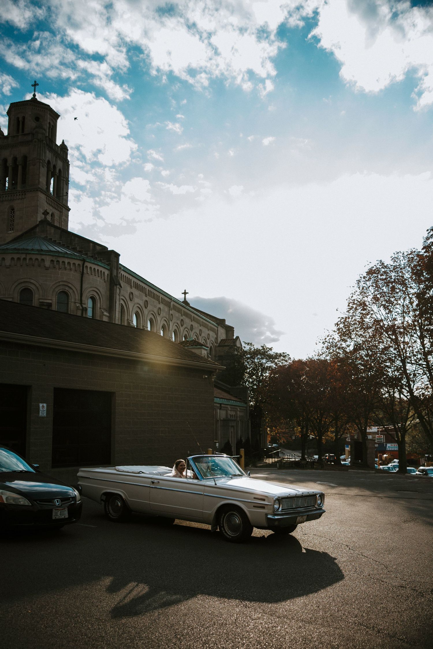 White vintage convertible parked outside a historic stone church with a cross under a dramatic sky at Urban Artifact in Cincinnati, Ohio