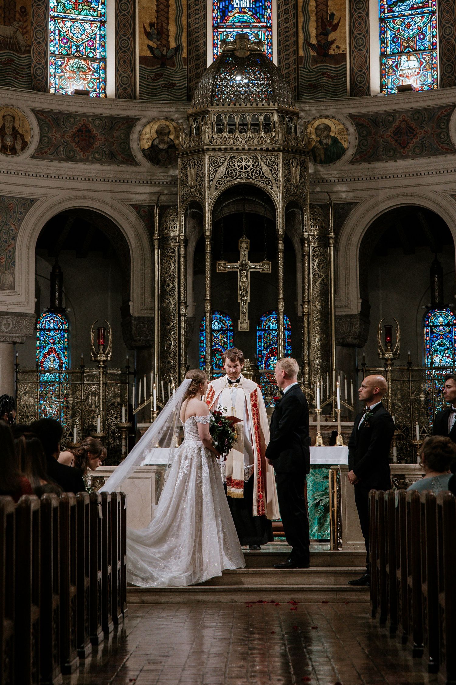 Bride and groom exchange vows at ornate altar with stained glass windows and decorative cross backdrop in Cincinnati, Ohio