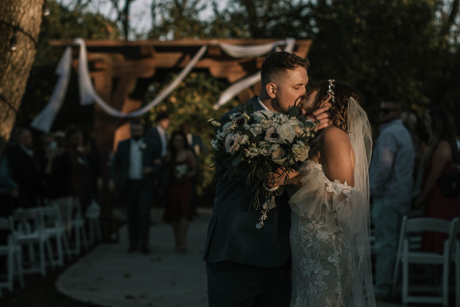 Bride and groom share romantic first kiss at outdoor evening wedding ceremony at Stone Valley Meadows in Dayton, Ohio