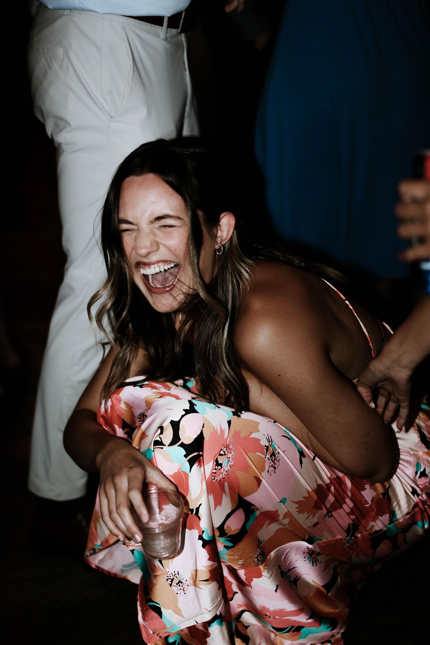 Woman in floral dress laughing joyfully while holding a drink at a wedding reception at Stone Valley Meadows in Dayton, Ohio
