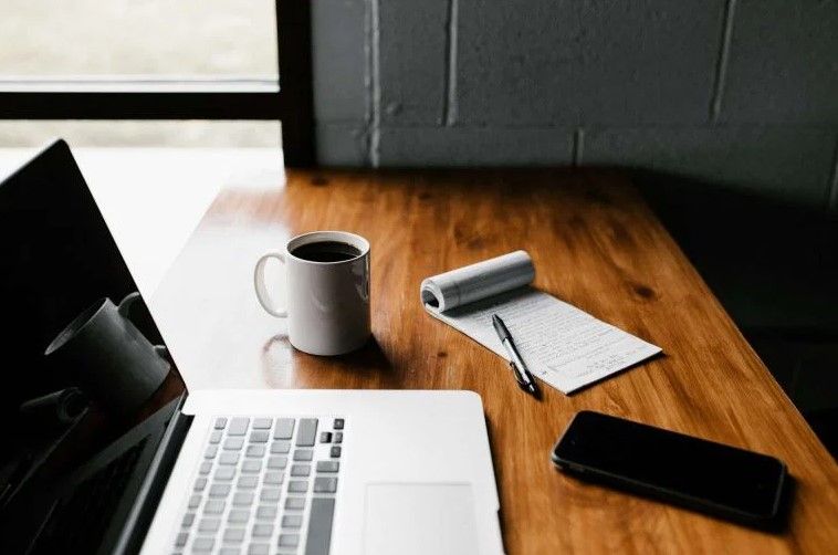 Minimalist workspace with open laptop, coffee mug, notepad, pen, and smartphone on wooden desk in Cincinnati, Ohio.