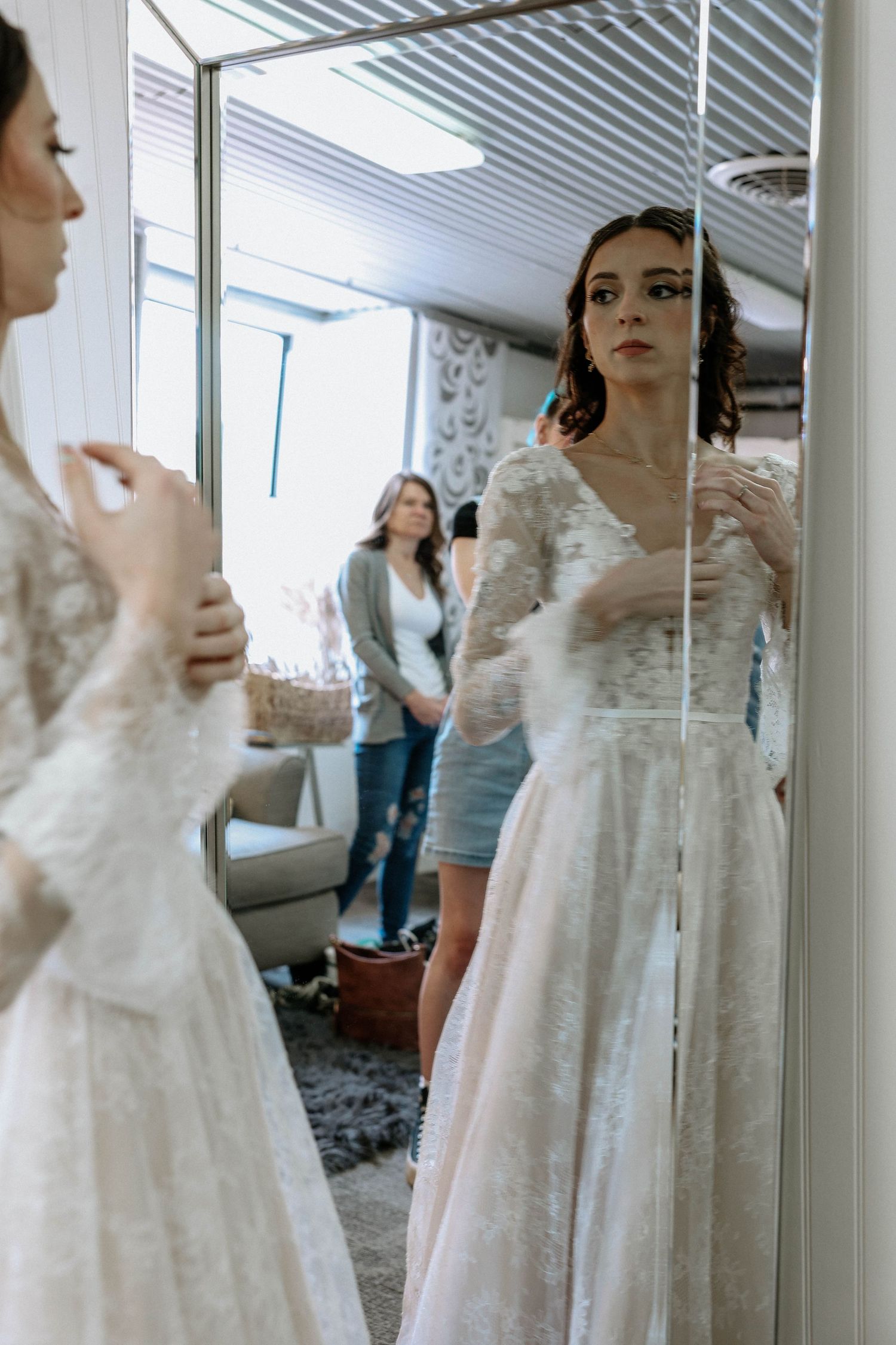 Bride in long-sleeve lace wedding gown admiring her reflection in a large mirror.