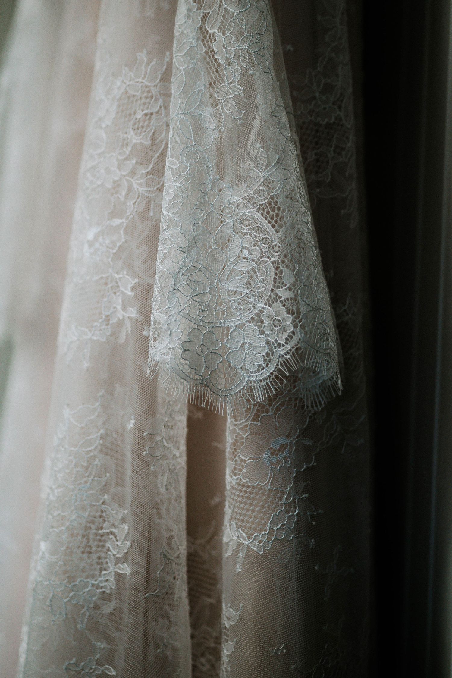 Close-up of delicate white lace wedding dress fabric hanging near a window.
