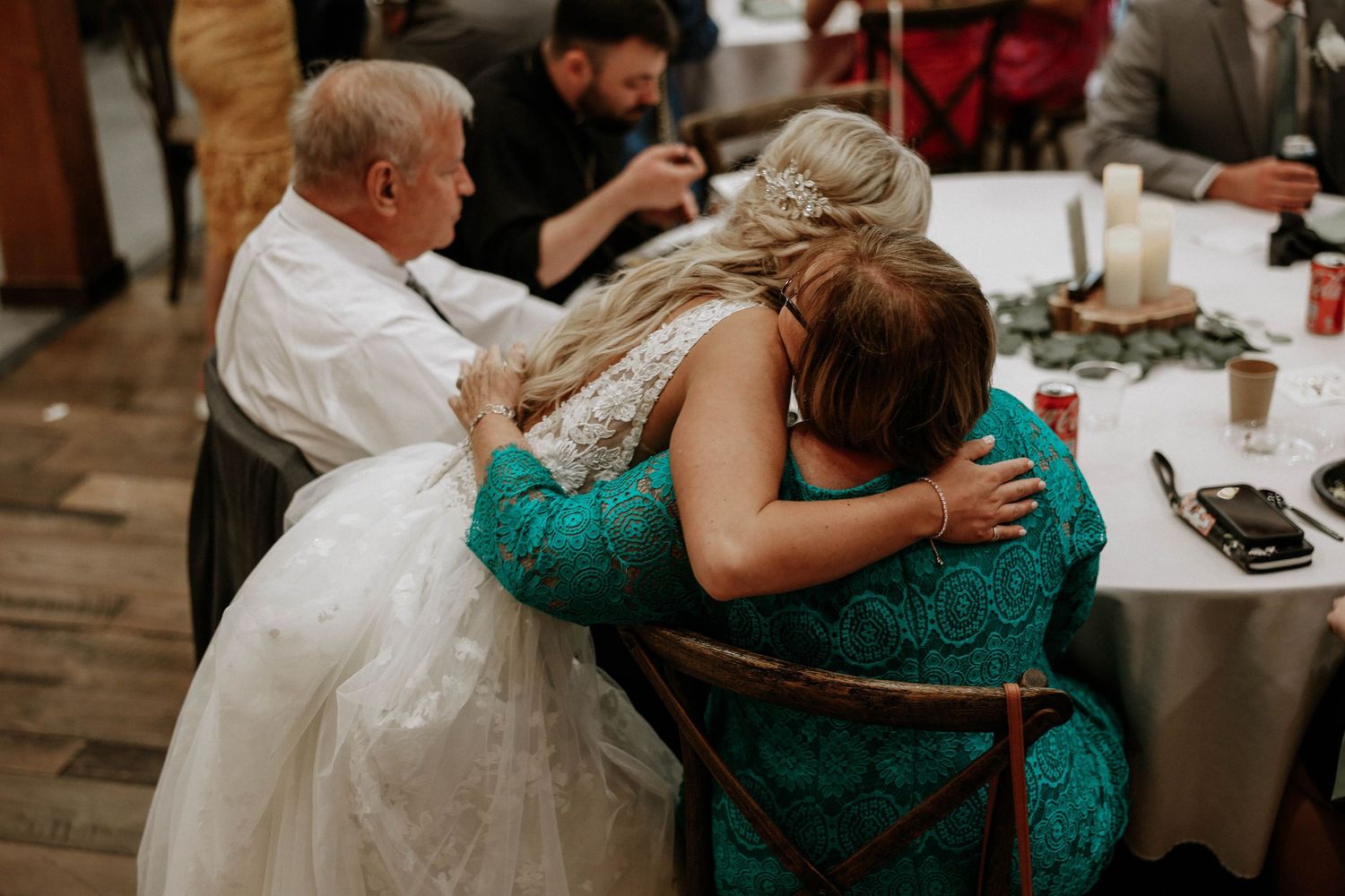 Bride sharing an emotional hug with a woman in teal at wedding reception.