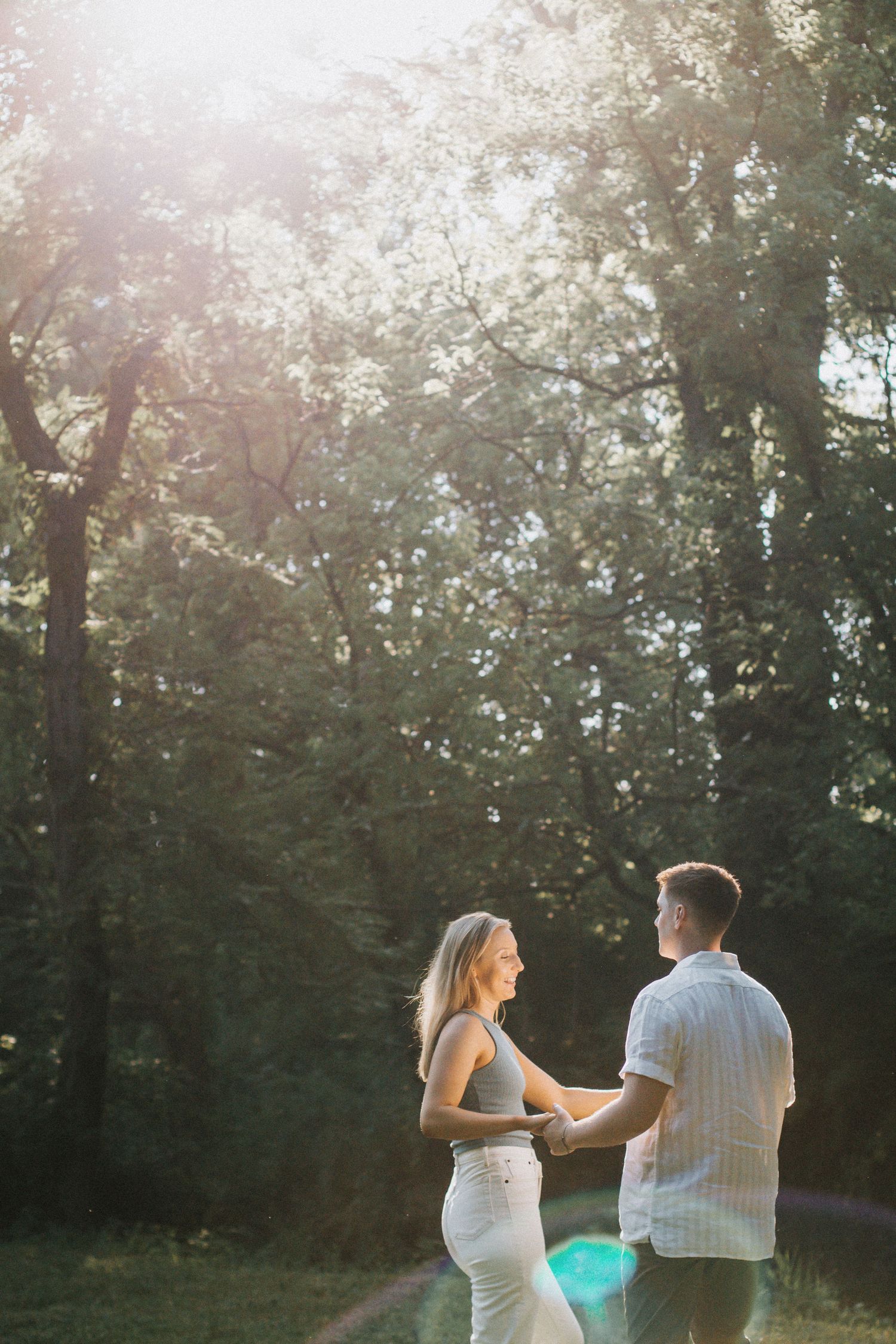 Couple holding hands and dancing in sunlit forest clearing with golden light streaming through trees in Columbus, Ohio