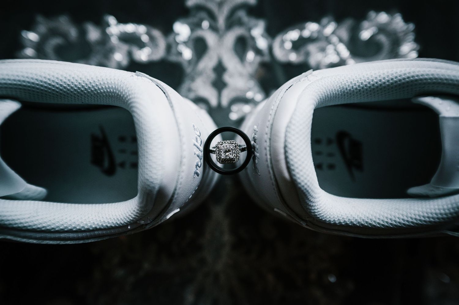 Diamond engagement ring creatively displayed between two white Nike sneakers on dark background at Central Park in New York City