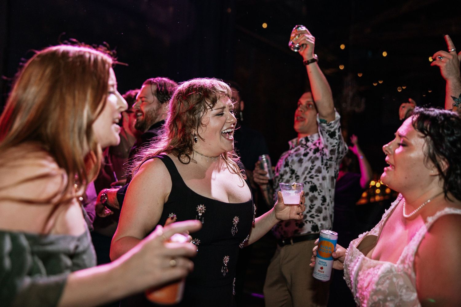 Group of women laughing and dancing together under pink lights at a wedding reception.
