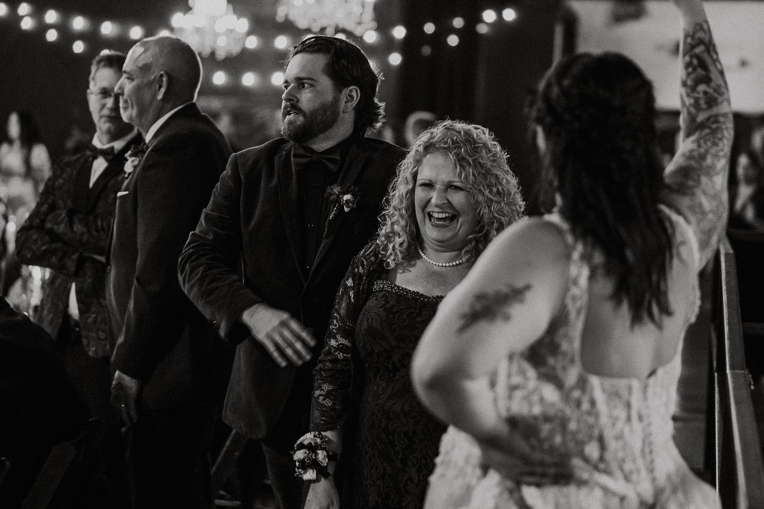 Black and white photo of joyful wedding guests laughing and celebrating on the dance floor.