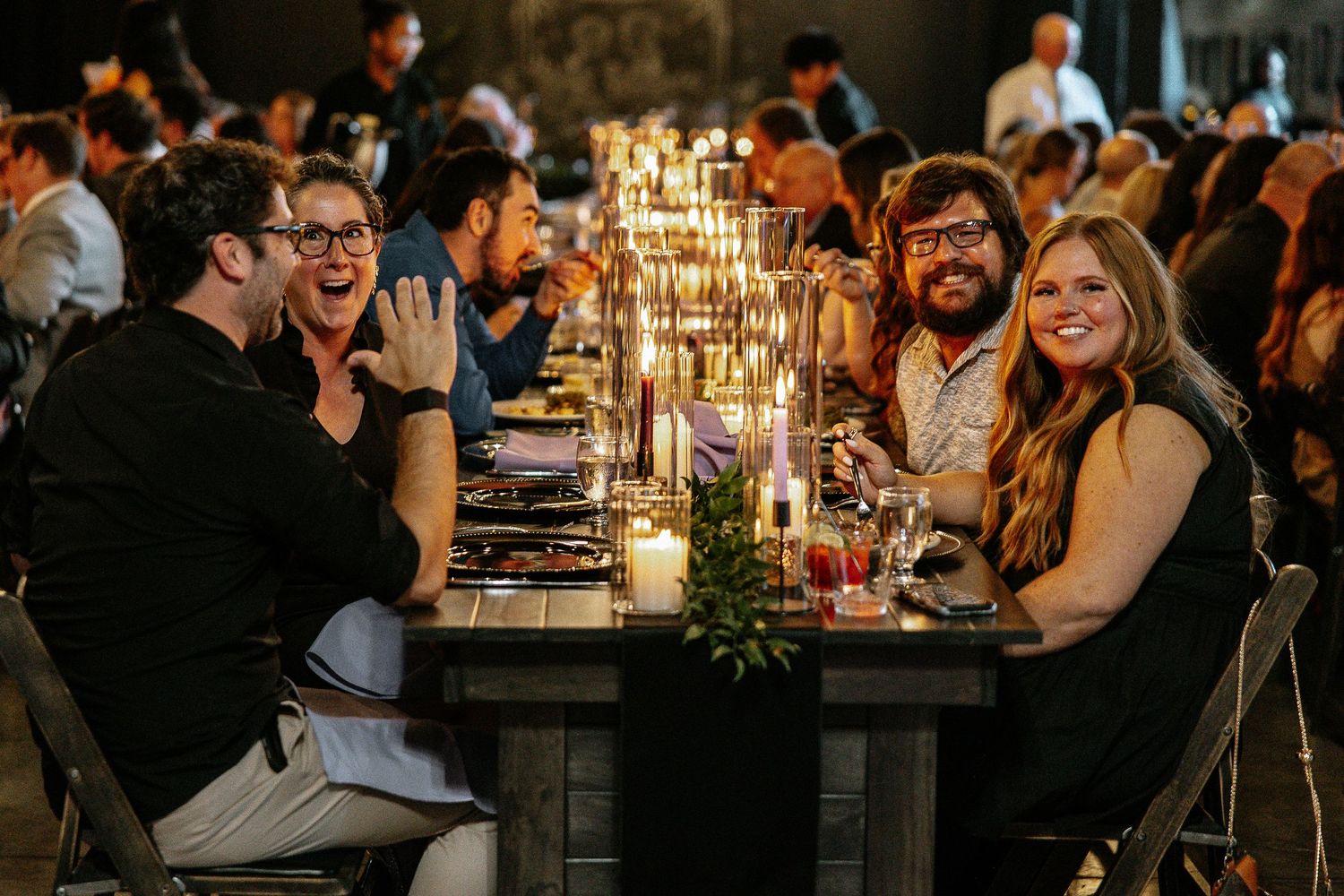 Joyful wedding guests laughing and celebrating together at a candlelit reception dinner table.