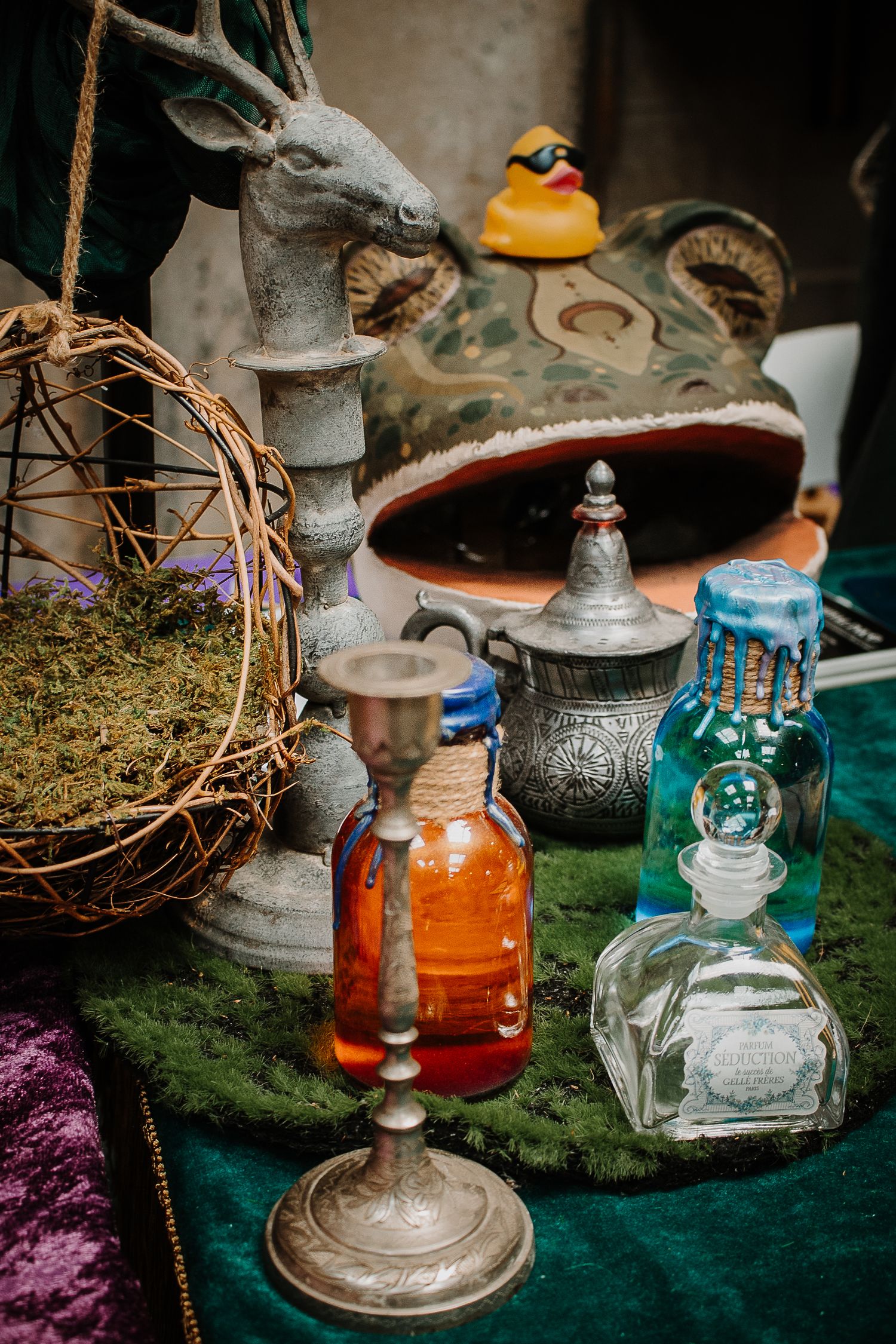 Antique bottles, deer statue, and mystical decor arranged on a green velvet table at a fantasy-themed display.