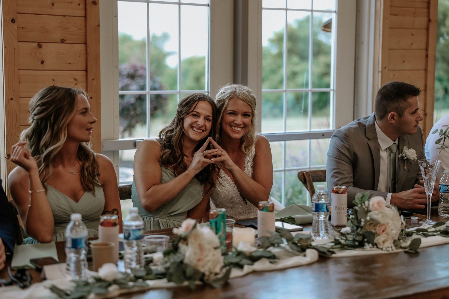 Bridesmaids laughing and smiling together at a wedding reception table decorated with flowers.