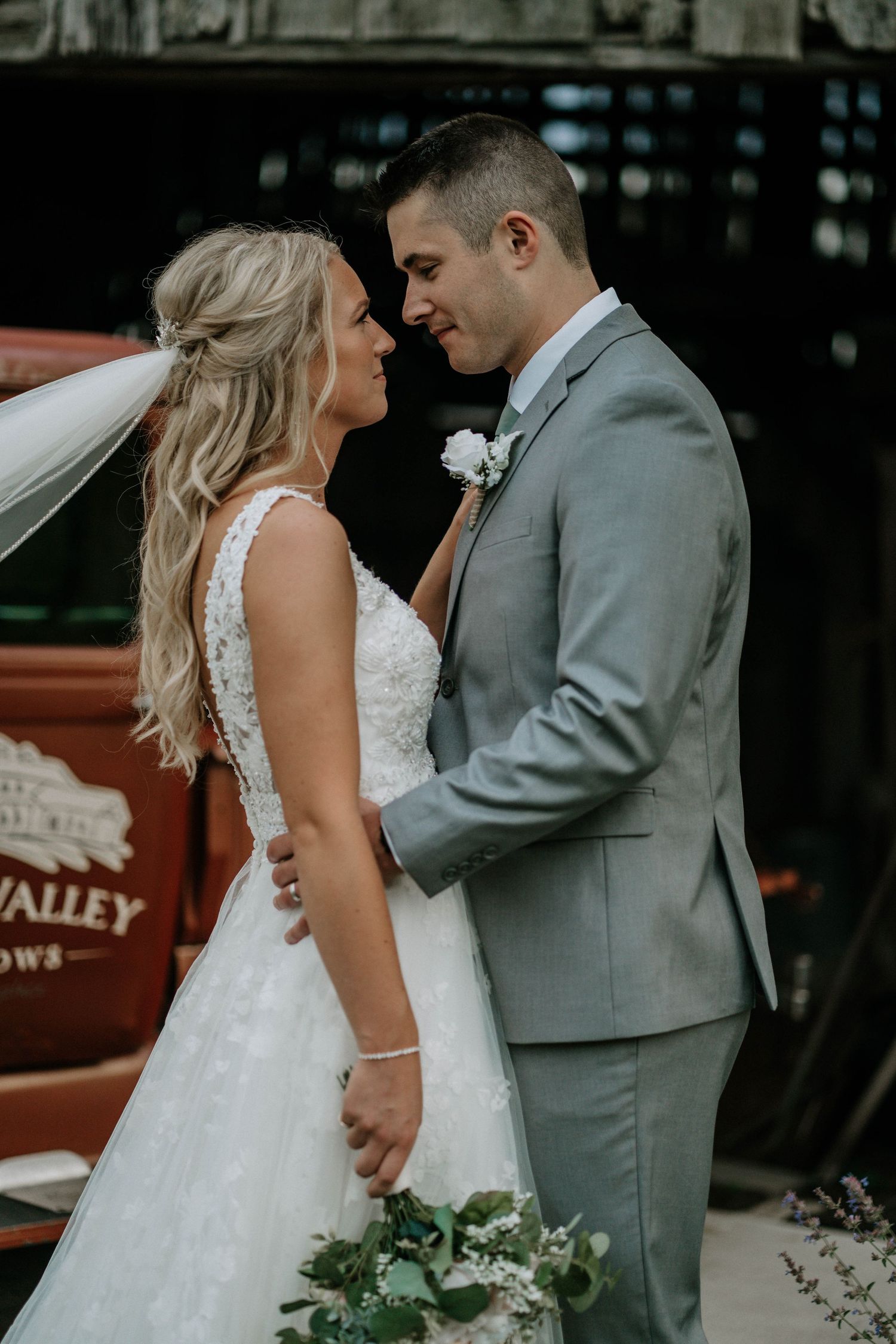 Bride and groom share a romantic moment in front of a red truck at their outdoor wedding venue.