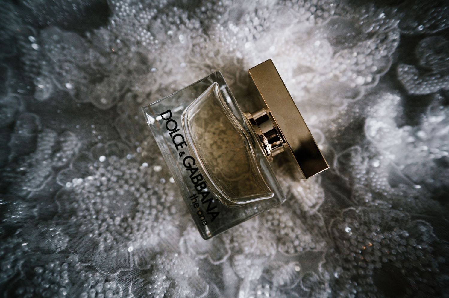 Dolce and Gabbana The One perfume bottle on white lace wedding dress fabric.