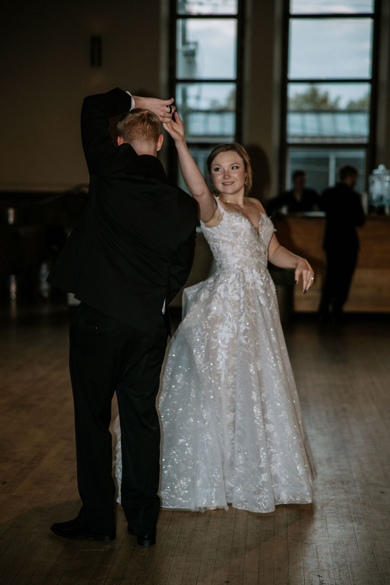 Bride in lace gown smiles as groom twirls her during first dance at wedding reception at Urban Artifact in Cincinnati, Ohio