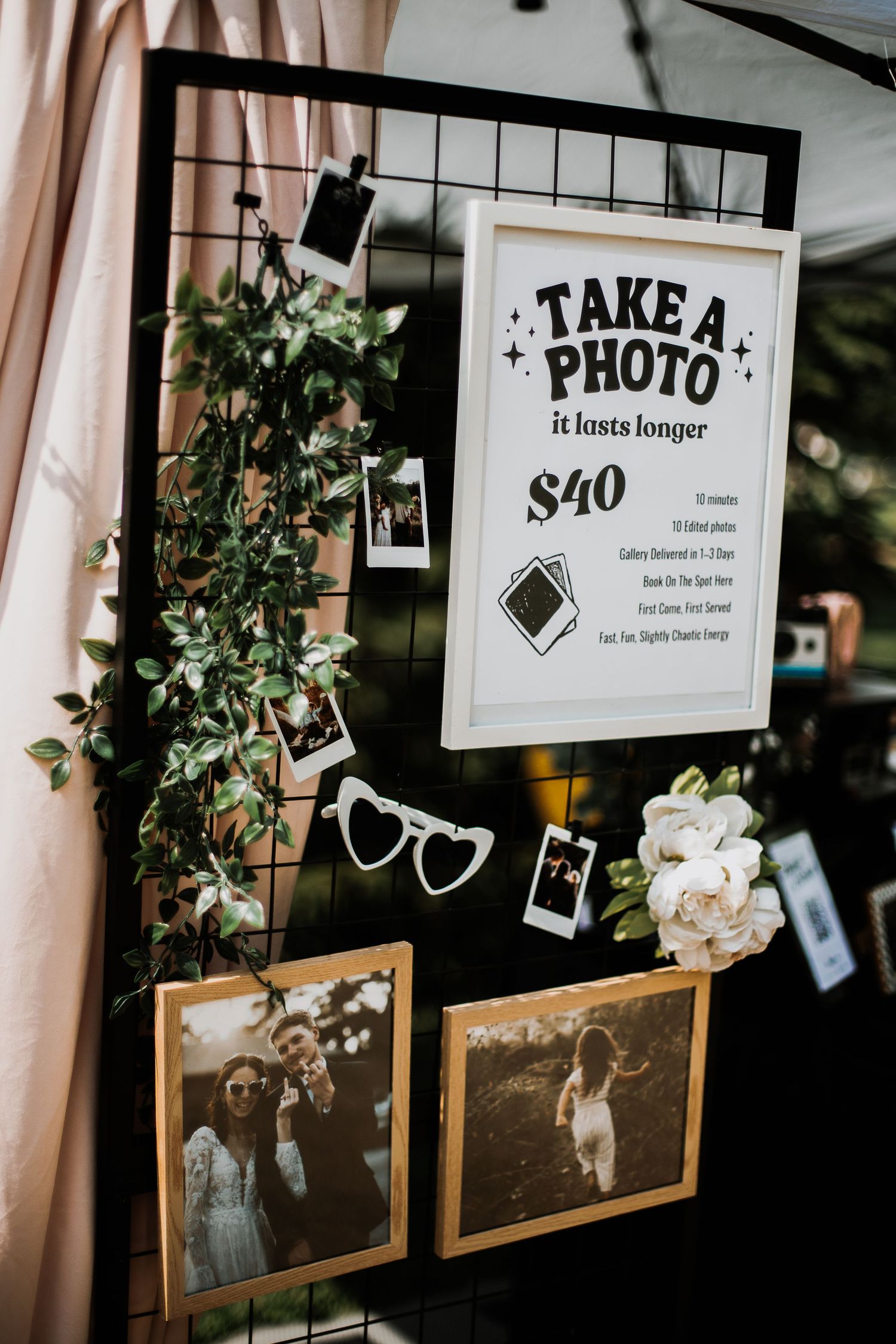 Wedding photo booth display with Polaroid photos, white flowers, and a Take a Photo sign offering prints for $40.
