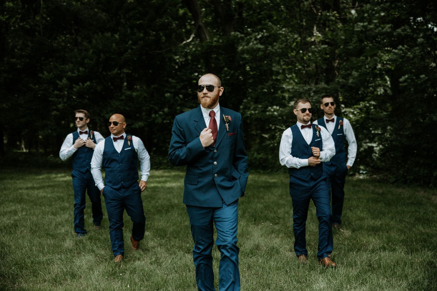 Groom and groomsmen in navy suits and sunglasses pose confidently on green lawn before wedding at The Barn at Wolf Creek in Akron, Ohio