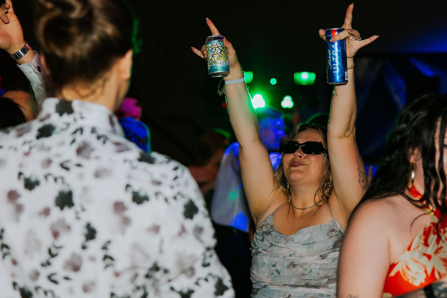Woman raises two cans overhead while dancing at lively wedding reception celebration.