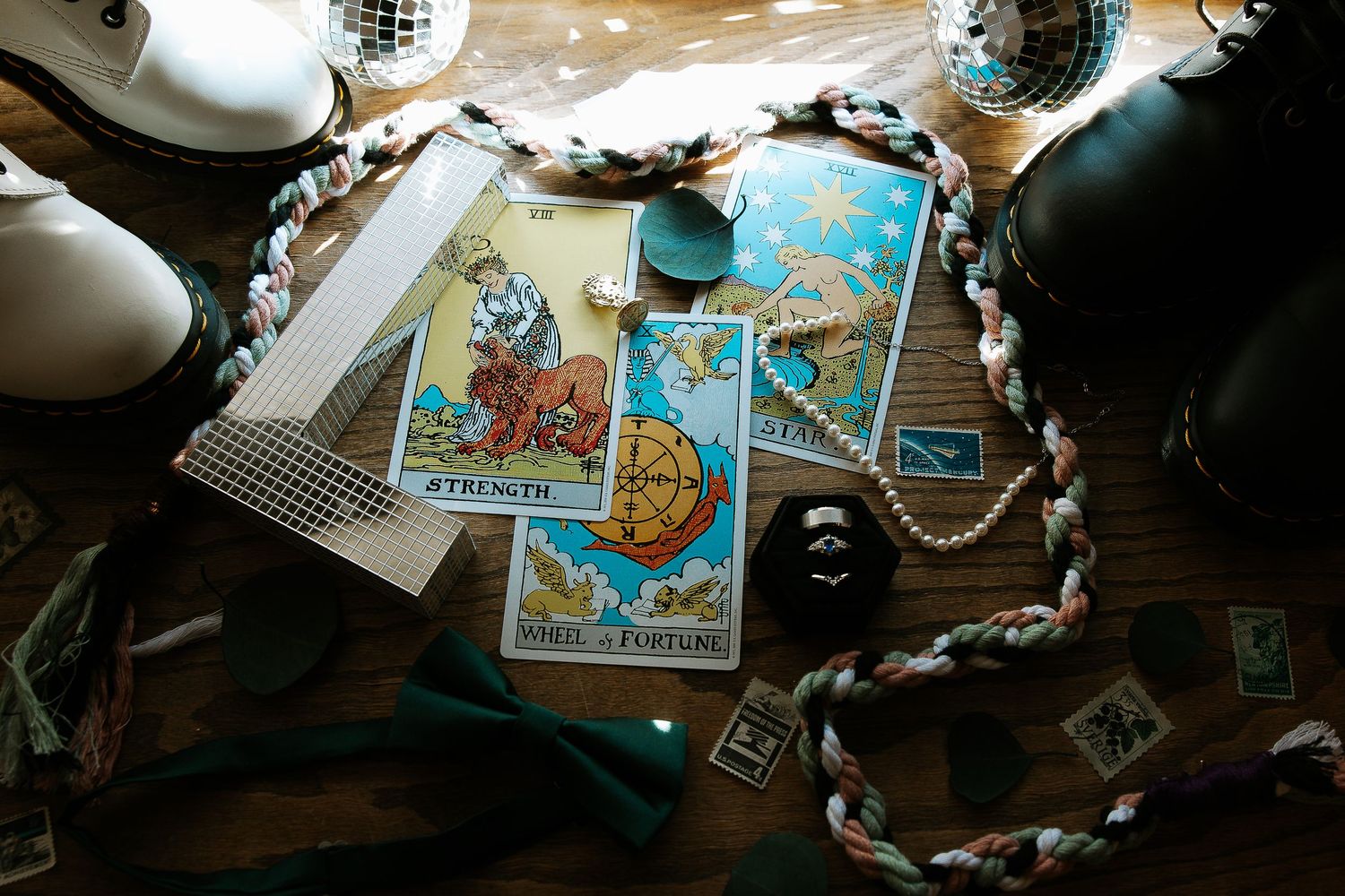 Tarot cards, bow tie, pearl necklace, and wedding accessories arranged on a rustic wooden table.