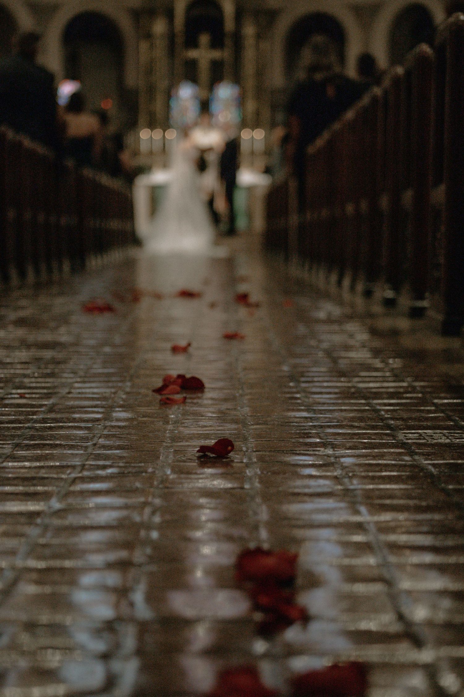 Red rose petals scattered along stone church aisle with bride and groom blurred in background in Cincinnati, Ohio