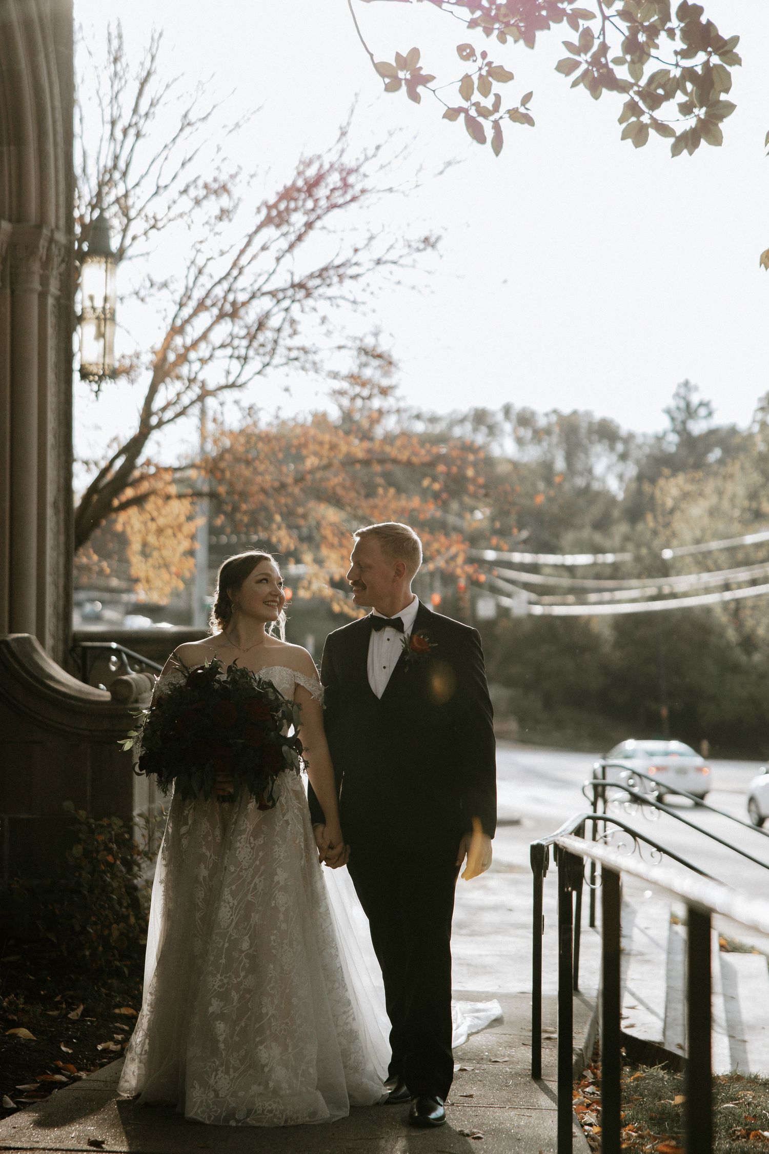 Bride and groom hold hands outside a historic church during fall wedding portraits with golden sunlight in Cincinnati, Ohio