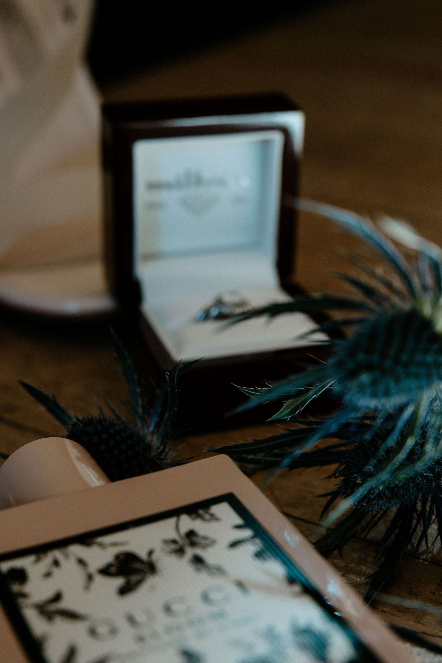 A diamond ring in a jewelry box surrounded by blue thistle flowers and a Gucci bottle at Urban Artifact in Cincinnati, Ohio
