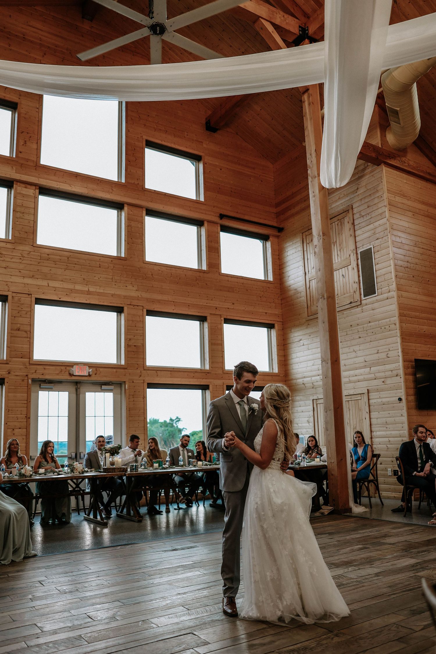 Bride and groom sharing first dance in stunning rustic barn venue with vaulted wood ceiling.
