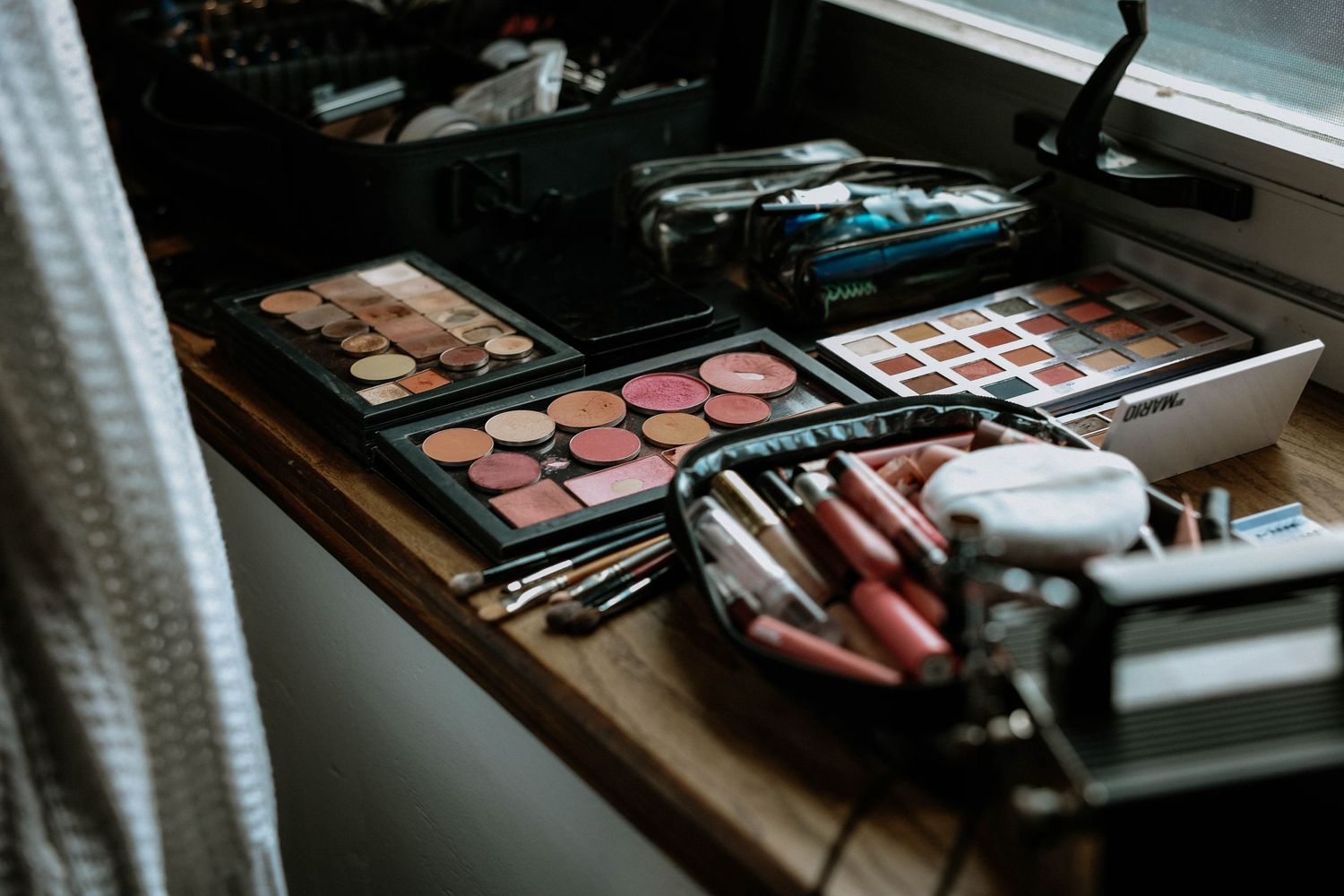 Professional makeup artist station with colorful eyeshadow palettes, blush, and brushes on a wooden vanity.