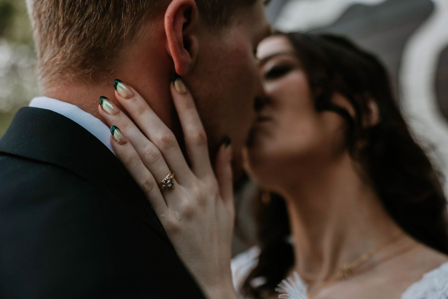 Close-up of a bride and groom sharing a kiss, showcasing her gold wedding ring and dark green manicure.