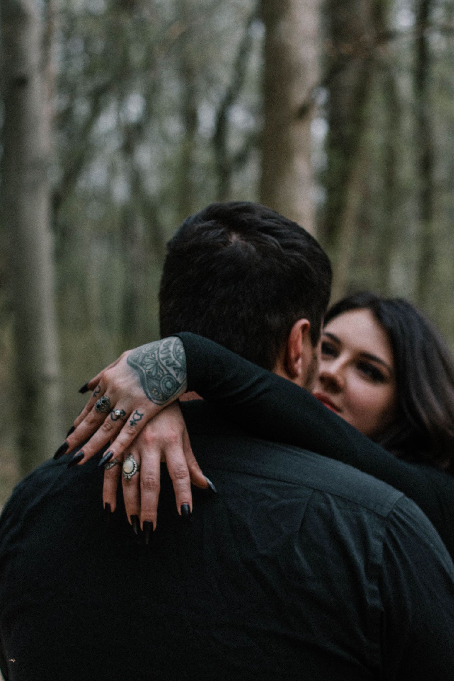 Couple embracing in forest, woman with black nails, rings, and hand tattoo visible over man's shoulder at French Park in Cincinnati, Ohio