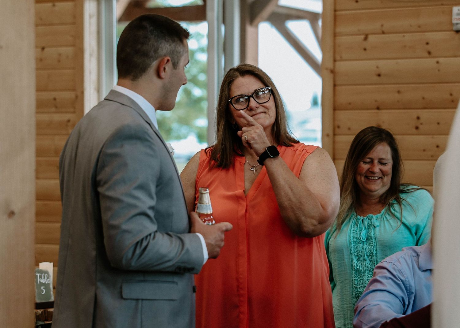 Two women smiling and laughing with a man in a suit inside a rustic wooden cabin venue.