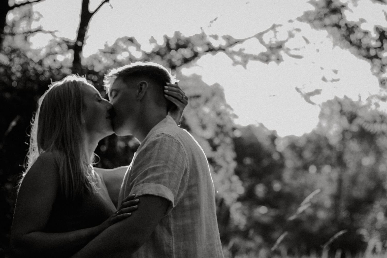 Black and white photo of a couple sharing a romantic kiss outdoors surrounded by blurred trees at Eden Park in Cincinnati, Ohio
