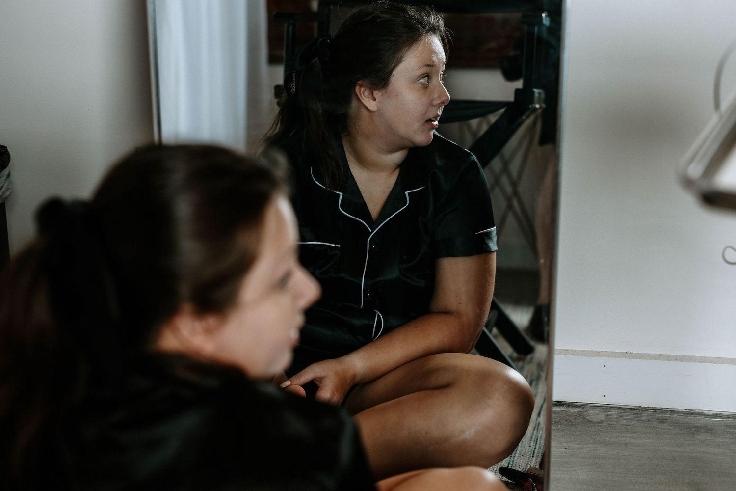 Two young women sitting on the floor indoors, engaged in conversation in a casual home setting.