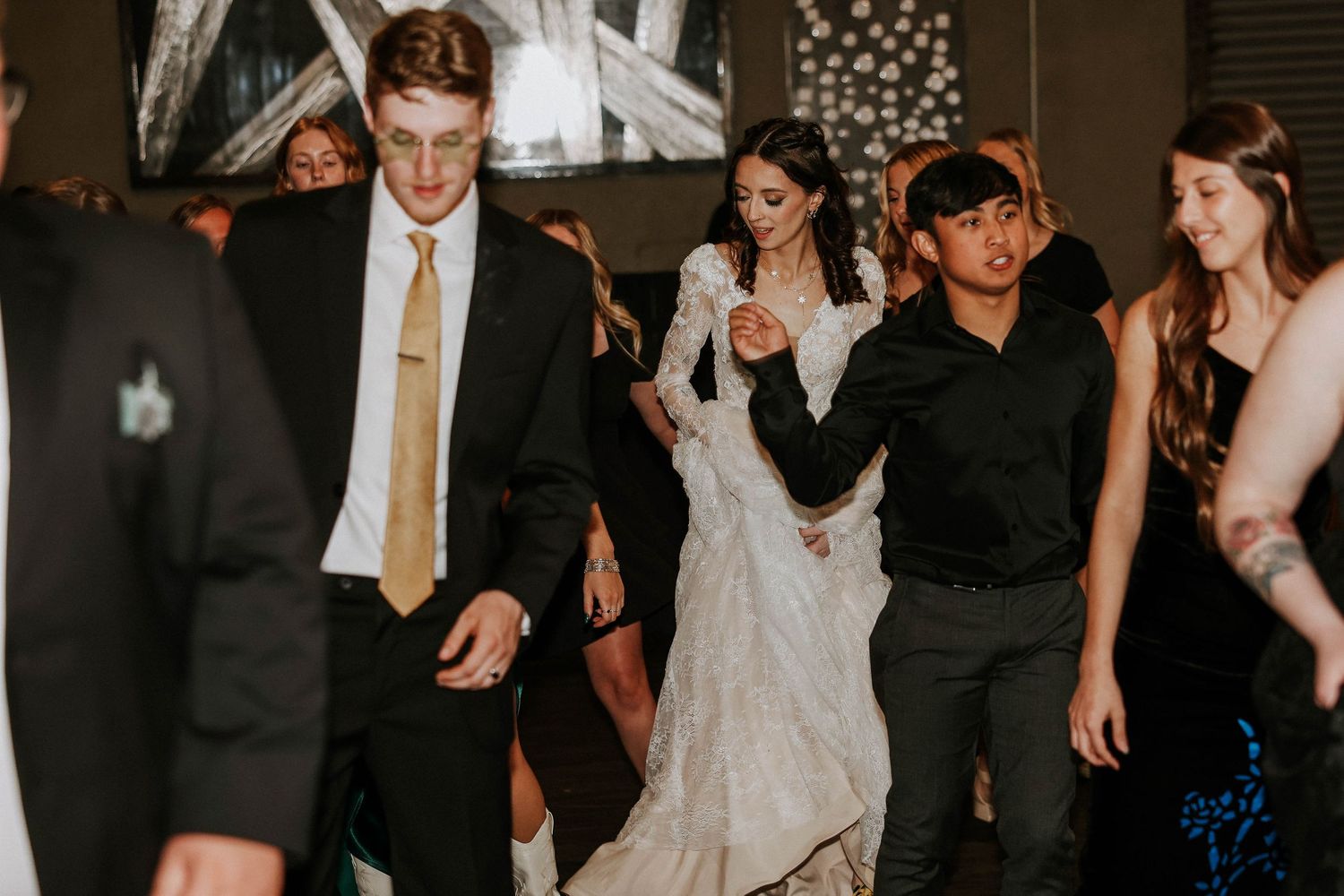 Bride in white lace gown dancing with guests at wedding reception celebration.